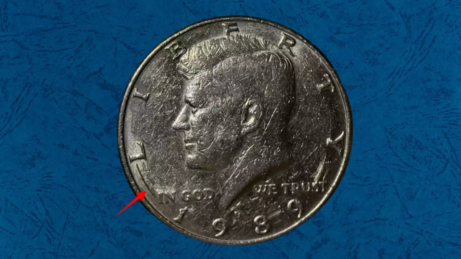 1989 Kennedy half dollar showing struck-through error with textured cloth impression visible on JFK portrait field area, caused by foreign material between die and planchet at striking